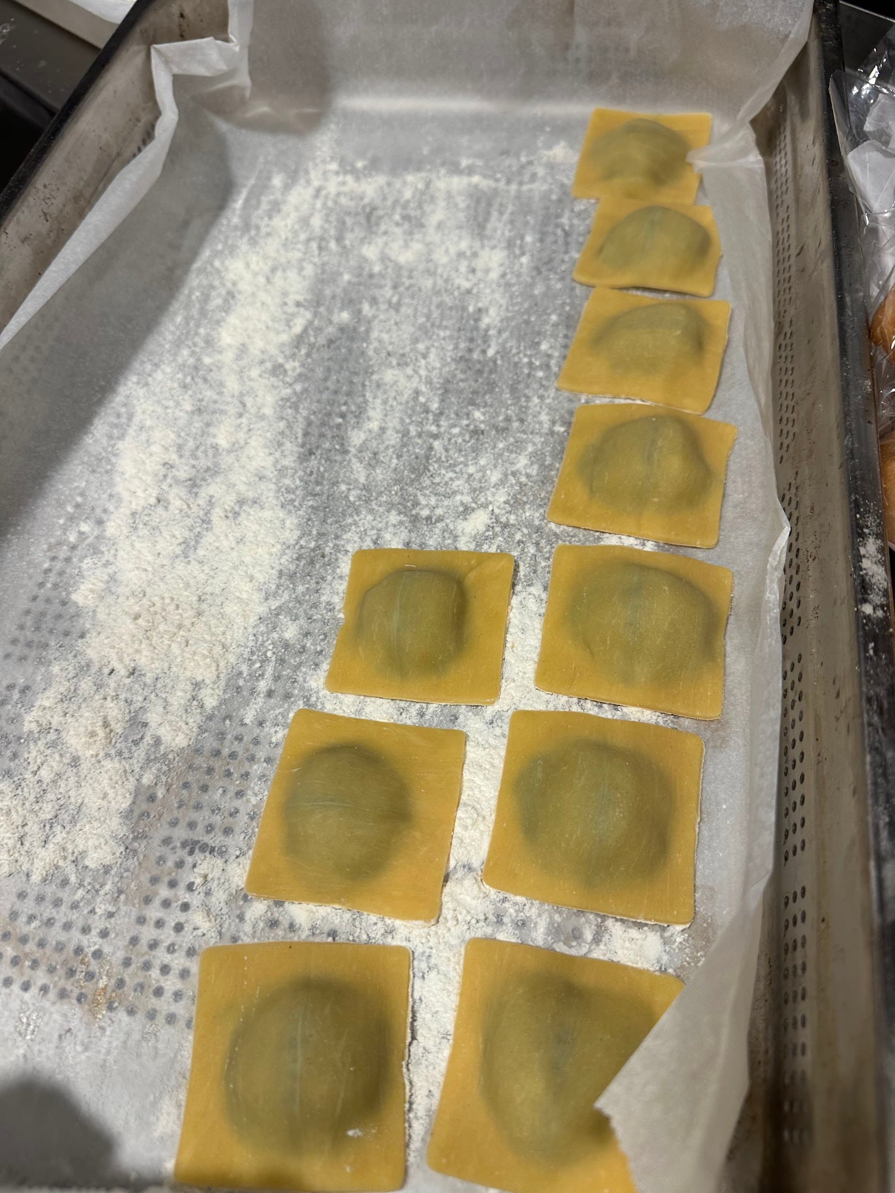 Ravioli crudos en fila sobre una bandeja enharinada